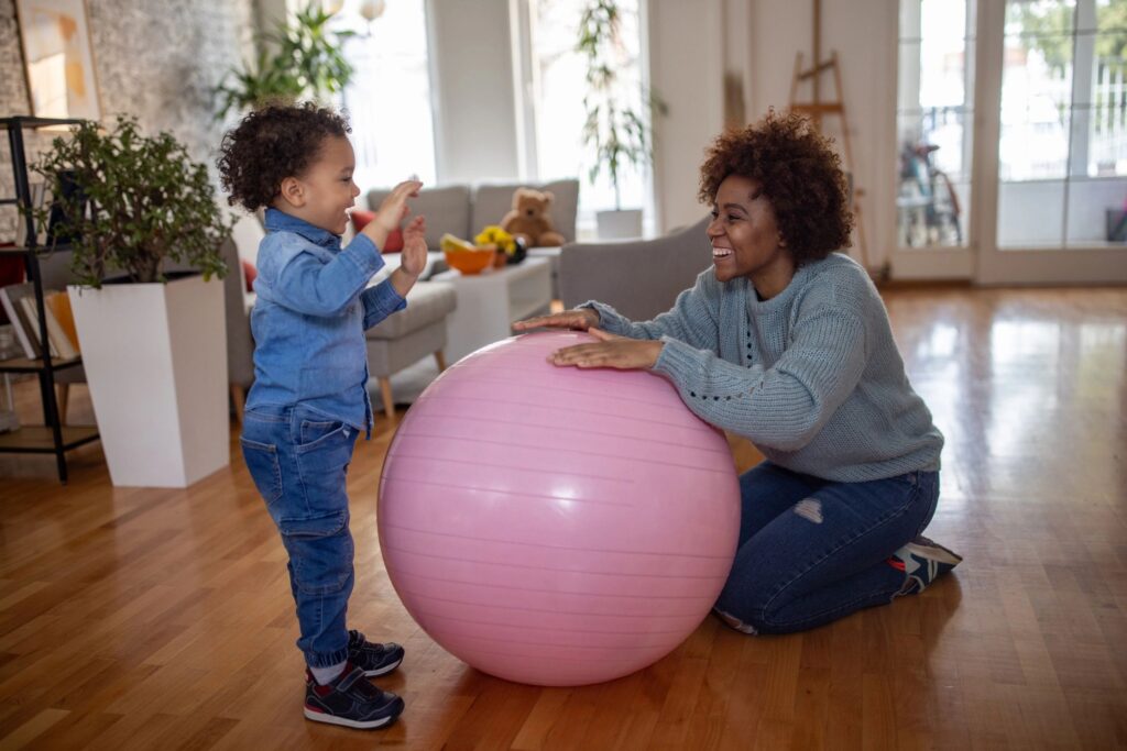 Playful mother and son Black ethnicity playing with a fitness ball