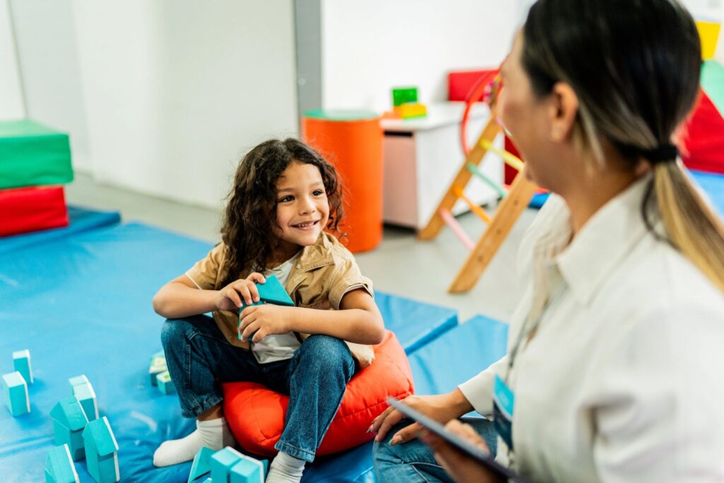 Child boy playing with cubes and talking to therapist during therapy at clinic